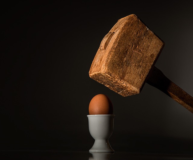 A wooden mallet prepares to strike a hard boiled egg in a cup