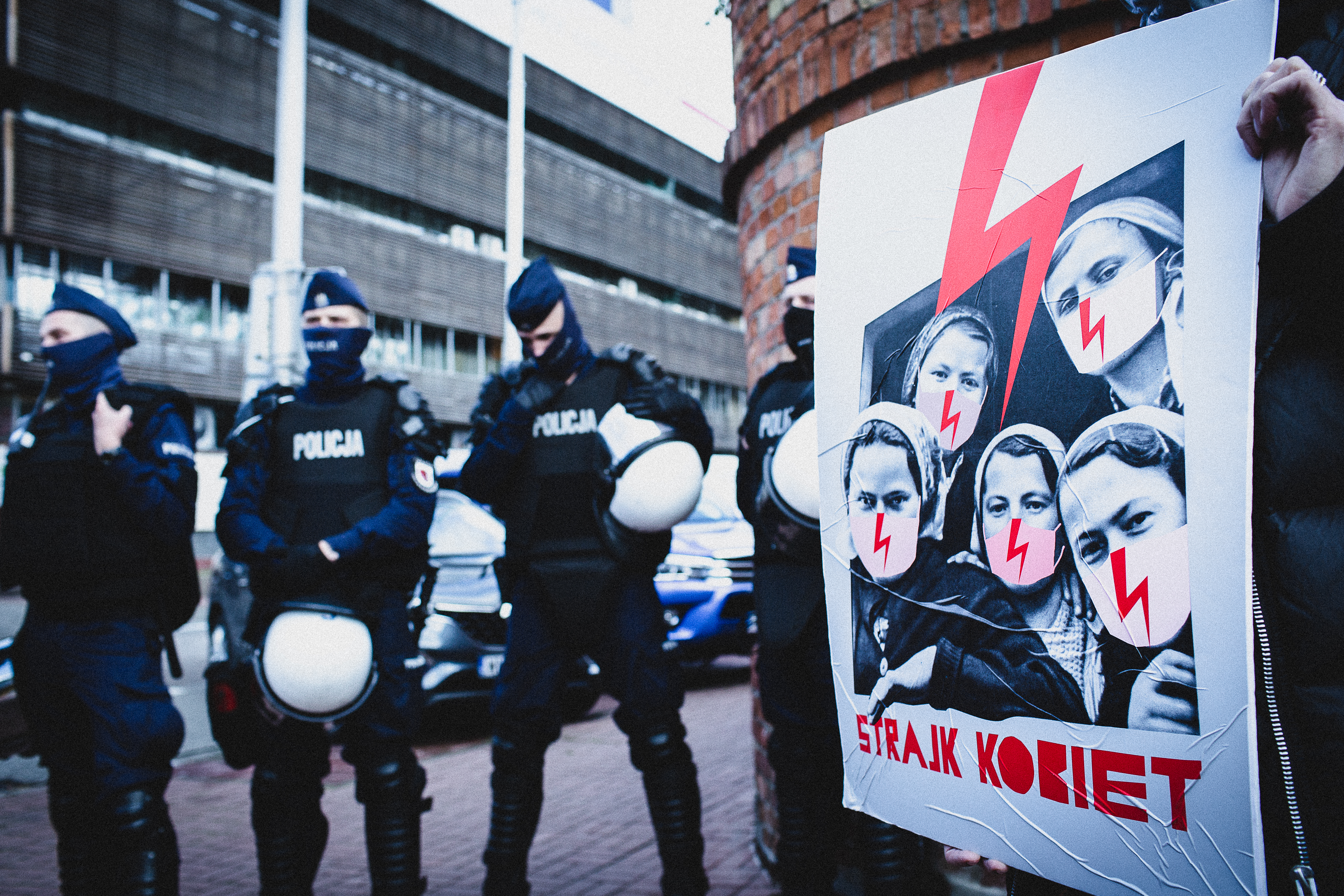 Protestor holding a Strajk Kobiet poster with police in the background. Women’s Strike protests, Warsaw, Poland. October 2020.